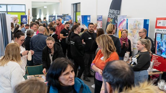 Ein Blick in einen Gang mit Ständen von verschiedenen sozialen Trägern, der gefüllt mit Besucher:innen ist.