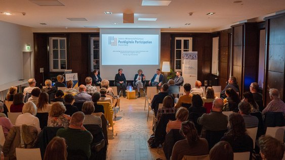 Blick von Hinten auf den vollen Saal und die Podiumsdiskussion.