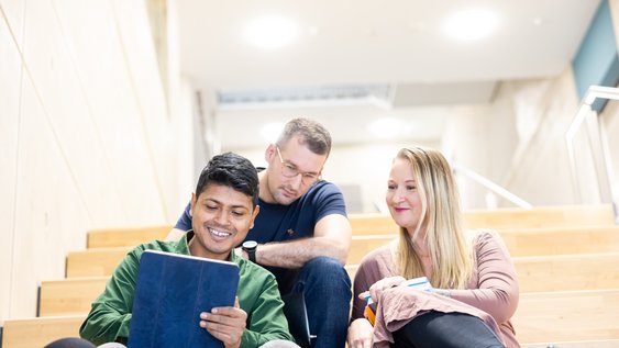 Studierende sitzen auf der Treppe und schauen auf ein Tablet