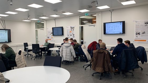 Studierende sitzen an Gruppentischen und lernen.