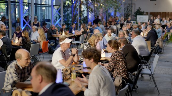 Wissenschaftler*innen und Besucher*innen sitzen sich beim Salon der Wissenschaft an Tischen gegenüber und sind im Gespräch.